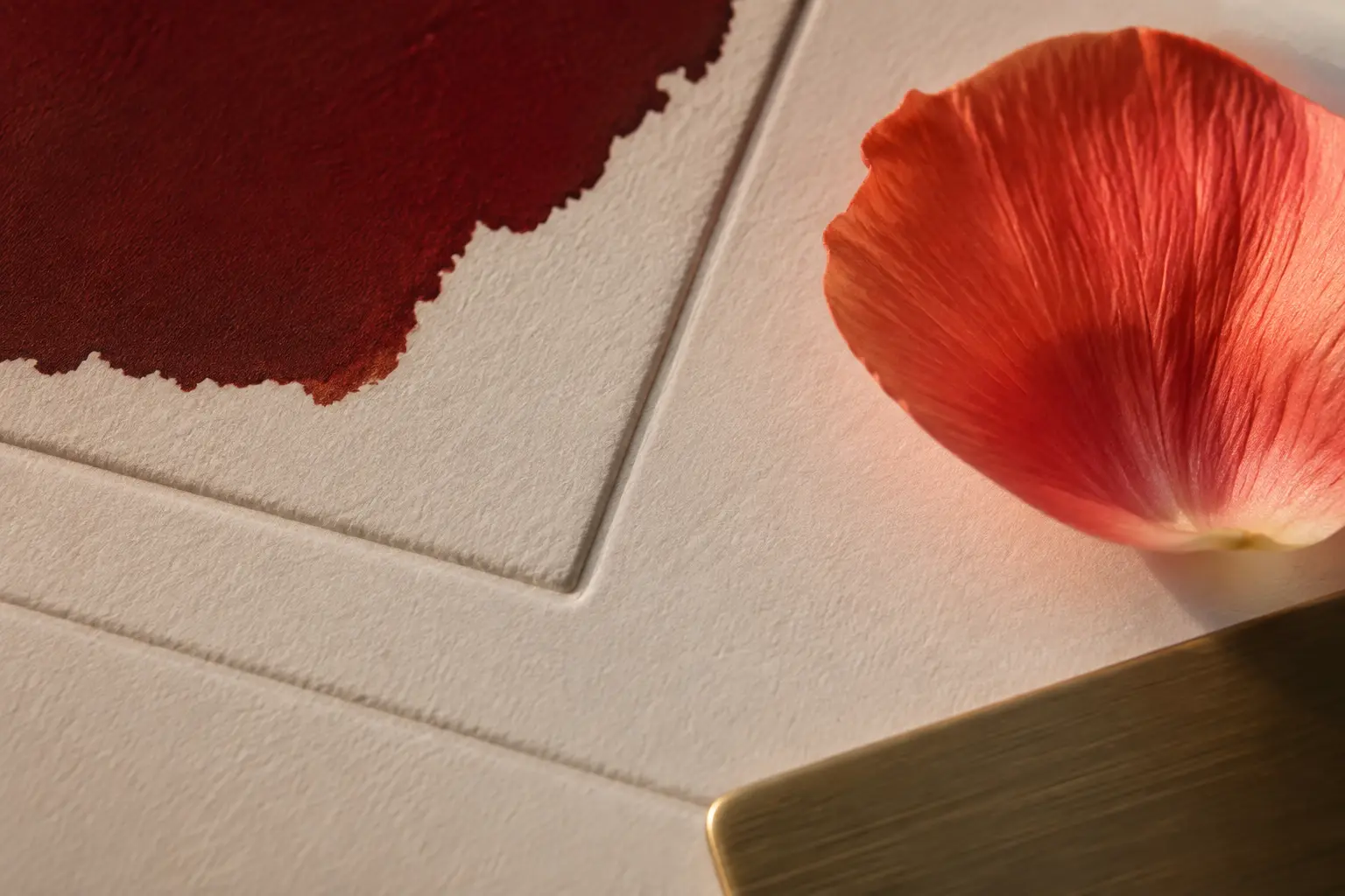 Textured ivory paper, burgundy ink and a coral flower petal in warm light